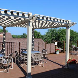 A sunny outdoor patio with a pergola and seating area on a wooden deck.