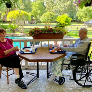Two elderly individuals enjoying a meal outdoors by the garden.