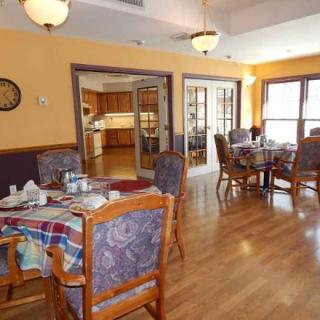 A cozy dining room with multiple tables and chairs, featuring wooden floors and warm lighting.