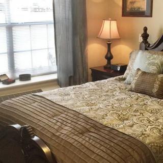 A cozy bedroom with a neatly made bed, decorative pillows, and a bedside lamp by the window.