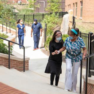 Healthcare workers assist a person as they walk together outdoors in a supportive environment.