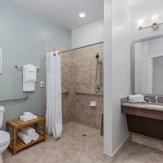 An accessible bathroom with a walk-in shower, toilet, sink, and neatly folded towels.