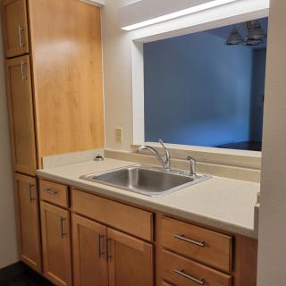 A kitchen area featuring wooden cabinets, a stainless steel sink, and a bright countertop.