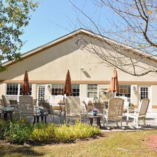 A sunny patio area with tables, chairs, and umbrellas in front of a building.