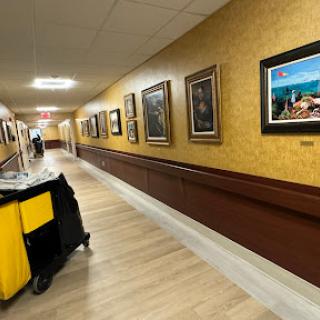 A well-lit hallway adorned with various framed artworks, featuring a cleaning cart in the foreground.