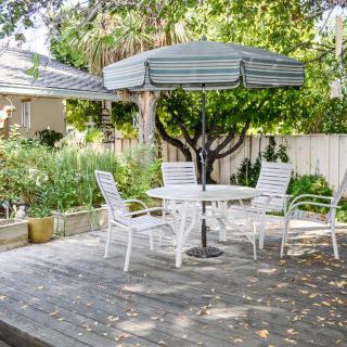 A sunny backyard patio featuring a table with an umbrella and several chairs, surrounded by lush greenery.