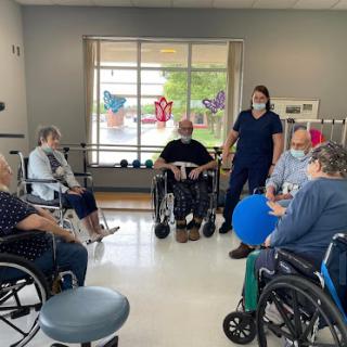 A group therapy session for elderly individuals in wheelchairs, guided by a healthcare professional.