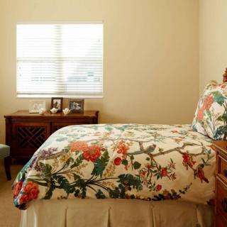 A cozy bedroom with floral bedding and natural light streaming through a window.