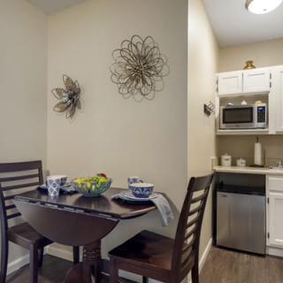 A cozy dining area with a small table and chairs adjacent to a compact kitchen featuring a microwave and fridge.