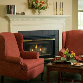 A cozy living room featuring a fireplace, red armchairs, and a wooden coffee table adorned with flowers and candles.