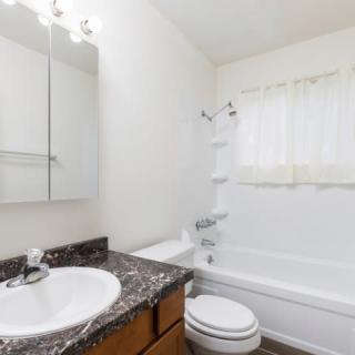A clean and simple bathroom with a granite countertop, bathtub, and white walls.