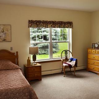 A cozy bedroom with a bed, dresser, and a window overlooking greenery.