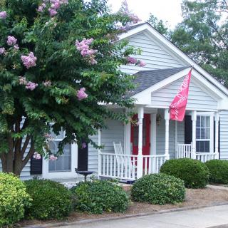 A small house with a porch, surrounded by greenery and displaying a red flag.
