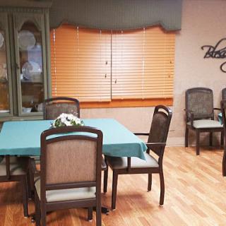 A cozy dining area featuring a table surrounded by chairs, with natural light filtering through the window blinds.