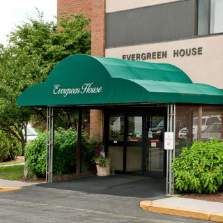 The entrance to Evergreen House, featuring a green awning surrounded by trees and bushes.