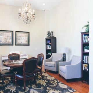 A cozy and elegant living room with classic furniture, featuring a central round table, upholstered chairs, two armchairs, bookcases, and a decorative chandelier.