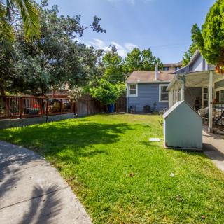 A sunny backyard with a well-maintained lawn and trees, featuring a small house and fence.