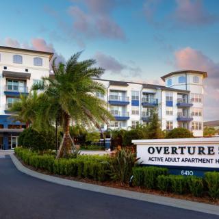 A modern retirement apartment complex with palm trees and landscaped surroundings.