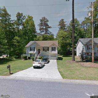 A suburban house with a driveway and cars parked, surrounded by trees.