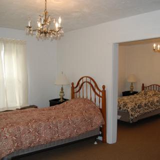 A cozy bedroom featuring two beds, a chandelier, and ample natural light.