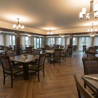An empty dining room with wooden tables and chairs, featuring elegant lighting fixtures and wood flooring.
