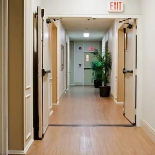 A well-lit hallway with open doors and an exit sign overhead.