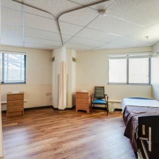 An empty room with a bed, desk, chair, and two windows.