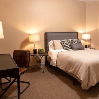 A cozy and minimalist bedroom with a comfortable bed, soft lighting from lamps, and a desk with a chair.