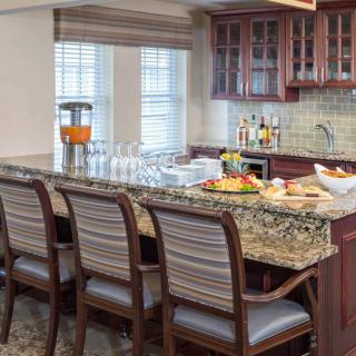A modern kitchen with a granite countertop and chairs, featuring a fruit platter and glassware.