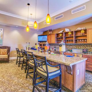 A cozy bar area featuring a spacious countertop with seating, ambient lighting, and decorative shelving.