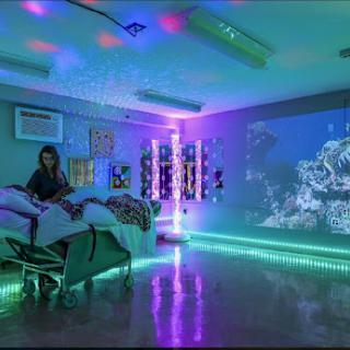 A vibrant and soothing patient room with colorful lighting and an underwater-themed projection, designed to create a calming atmosphere.