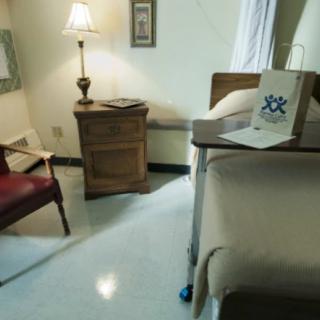 A clean and minimalistic hospital room with a bed, lamp, chair, and nightstand.