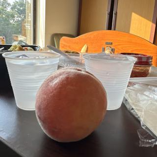 A peach in the foreground with two cups of water on a table.