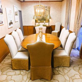 A well-decorated dining room featuring a large wooden table surrounded by upholstered chairs, with a chandelier overhead and framed artwork on the walls.