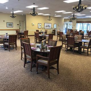 An empty dining room with multiple tables and chairs neatly arranged on a carpeted floor.