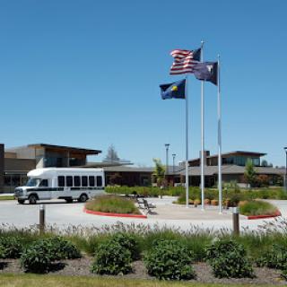 A serene exterior view featuring a bus, multiple flags flying, and landscaped grounds under a clear blue sky.