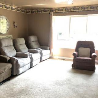 A cozy living room with a row of recliner chairs and a single armchair by the window.