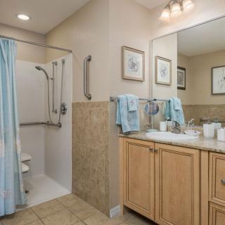 A clean and organized bathroom with a shower, large mirror, and wooden cabinets.