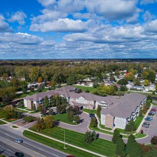 Aerial view of a residential building complex surrounded by roads and trees under a cloudy sky.