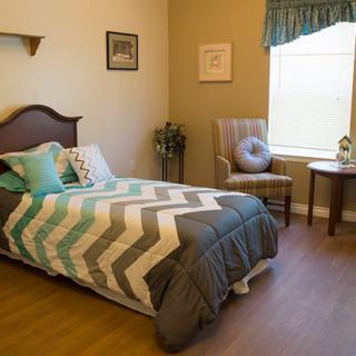 A cozy bedroom with a chevron-patterned bedspread, a chair by the window, and decorative elements.