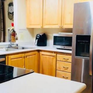 A modern kitchen with wooden cabinets, featuring a refrigerator, microwave, and coffee maker.