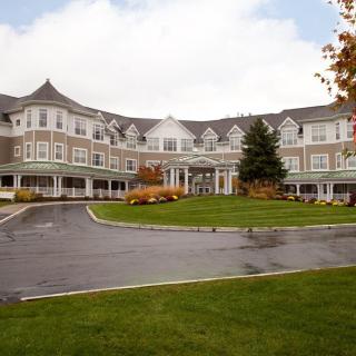 A large, elegant building with multiple gables and a landscaped driveway surrounded by autumn foliage.