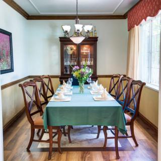 A neatly set dining room with a table and chairs, adorned with a floral centerpiece under a chandelier.