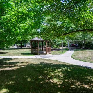 A peaceful park scene with a gazebo surrounded by pathways and lush green trees.