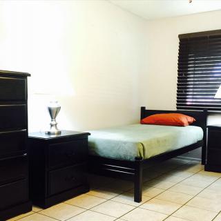A minimalist bedroom with a single bed, dresser, nightstand, and lamp.