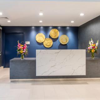 A modern reception area featuring a marble desk, decorative wall art, and floral arrangements.
