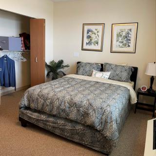 A cozy bedroom with a neatly made bed, artwork on the wall, and an open closet.