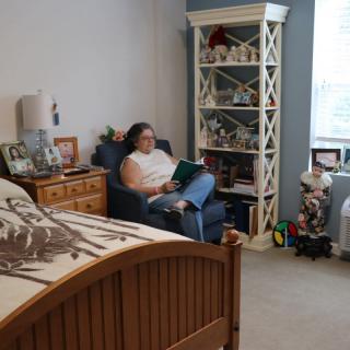 A person sits reading in a cozy bedroom with a bookshelf and decorations.