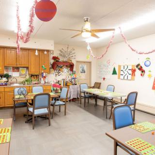 A decorated dining area with tables and chairs, featuring holiday decorations and a small kitchen space.