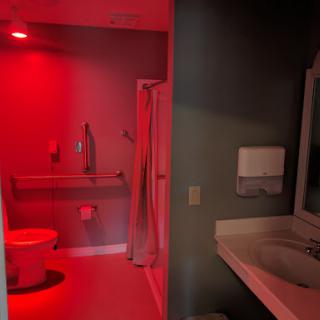 A visually striking bathroom illuminated with red light, featuring essential amenities like a toilet, sink, and shower.